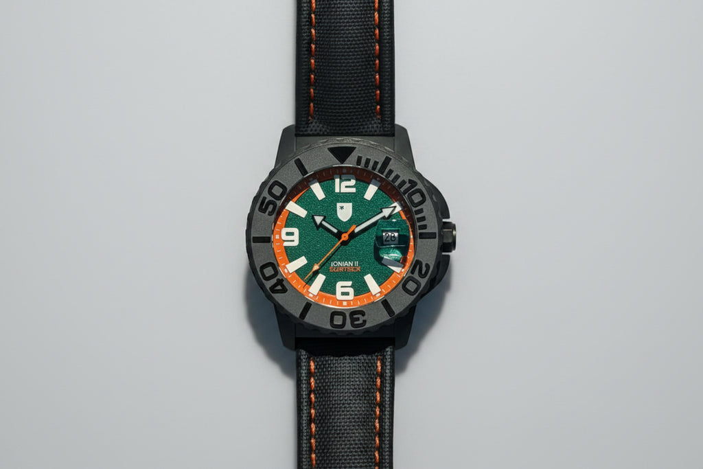 Watch with a green face and black strap on a pebbled surface